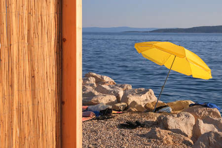 Yellow beach umbrella on summer coast. Sea beach with sun parasol is waiting for tourists on Sunset. Happy summer vacations concept. Vertical view.の写真素材