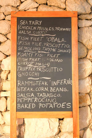 Chalkboard menu black color, message or advertising. Blackboard is standing near the restaurant in sea coast. Sunny day.の写真素材