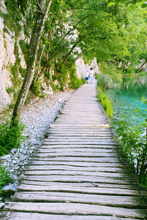 Summer landscapes along green lake in traveling journey. Wooden bridge walkway. Tourist walk.