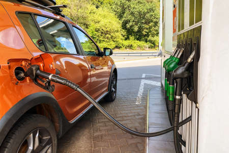 Pumping gasoline fuel in orange car at a gas station. Fill car with fuel in petrol station. Close...