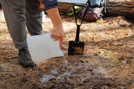 Black shovel in human hands. Tourist digs soil with a shovel in the forest.