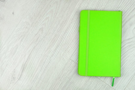 Green notebook on a wooden light background. Closed. Top view.の写真素材