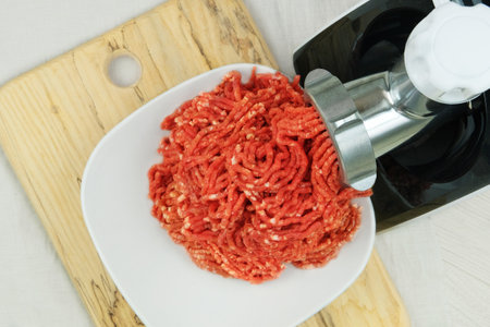 Bowl of mince with electric meat grinder in kitchen interior. Homemade minced meat comes out of the...