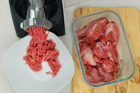 Mince meat in bowl with electric meat grinder in kitchen interior. Homemade minced beef comes out of...