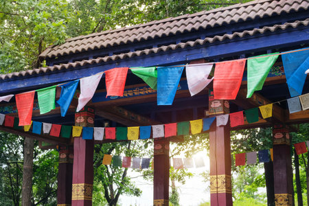 Buddhist prayer flags on wind on background of trees. Sunshine visible through numerous colorful...