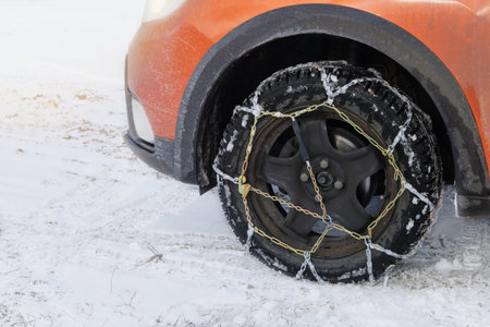 Vehicle equipment for off-road and bad weather. Chains on wheel of orange car in winter in outdoor.