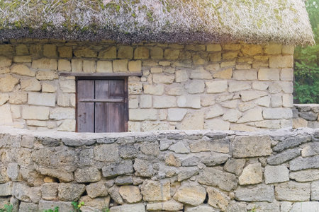 Old rural house with thatched roof and stone bricks. European village is preserving rustic traditions and culture. Sunny day.