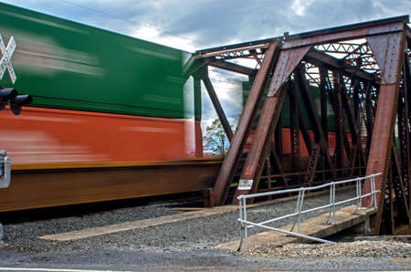 Red and green train cars in motion crossing bridge.の写真素材