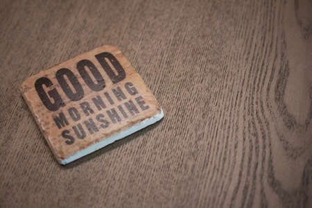 A stone coaster on a wooden table surface reading Good Morning Sunshineの写真素材