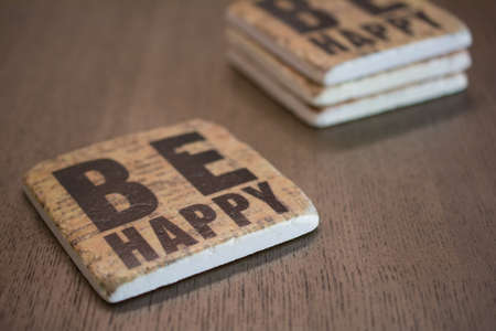 A set of stone coasters stacked on a wooden table surface reading Be Happyの写真素材