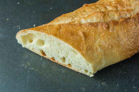 Cut bread baguette on black surface angled view
