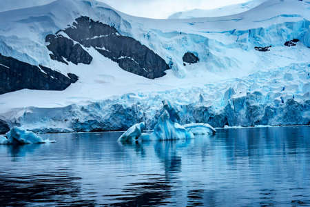 Snowing Red Kayaks Iceberg Blue Glacier Paradise Harbor Bay Antarctic Peninsula Antarctica.  Glacier ice blue because air squeezed out of snow.の写真素材