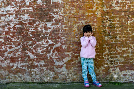 Asian female child wearing pink jacket cute pose with old brick wall backgroundの写真素材