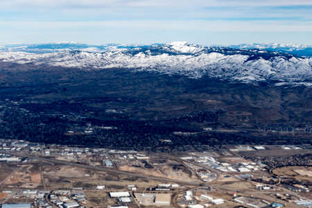 Aerial View of Idaho mountains from the sky while inside an airplane. View of brown mountains and trees covered with snowの写真素材