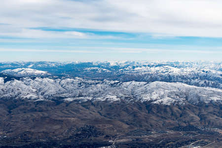 Aerial View of Idaho mountains from the sky while inside an airplane. View of brown mountains and trees covered with snowの写真素材