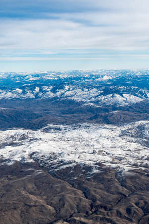 Aerial View of Idaho mountains from the sky while inside an airplane. View of brown mountains and trees covered with snowの写真素材