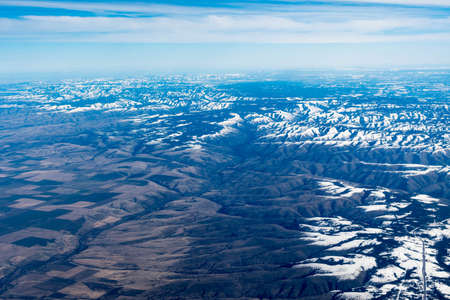 Aerial View of Idaho mountains from the sky while inside an airplane. View of brown mountains and trees covered with snowの写真素材