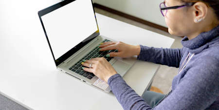 Portrait of middle age woman using her blank screen laptop while sitting back to back on the dining...
