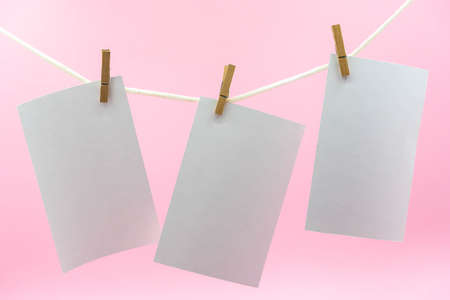 Multiple empty paper sheet for notes that hang on a rope with clothespins and isolated on pink....