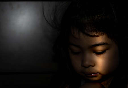 Powerful shot of a sad asian child. Female asian child sad dark sceneの写真素材