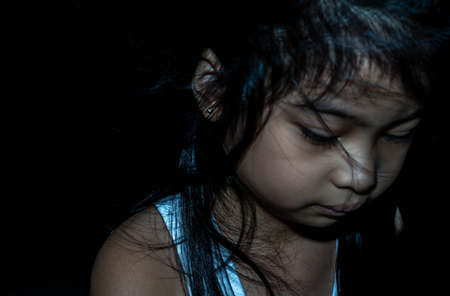 Powerful shot of a sad asian child. Female asian child sad dark sceneの写真素材