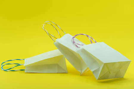 Colourful paper shopping bags isolated on Yellow Background. Closeup shot of white shopping bags