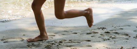 A child runs along the river bank splashing water with his feet. In summer, the child plays on the beach, runs barefoot on the sand. Sea tour. Children's feet in the sandの写真素材