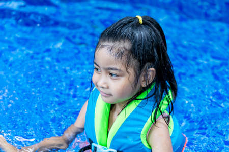 Pretty asian child smilling while wearing a vest in a swimming pool during swimming lesson