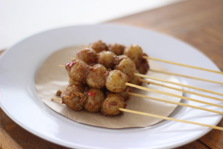 Close-up shot of traditional Indonesian bakso tusuk, or skewered meatballs, presented on a white...