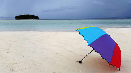 Colorful umbrella laying down in foreshore surrounded by white sand and blue beachの写真素材