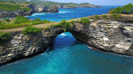 Huge coral with big hole and green bush on the top surrounded by blue waterの写真素材