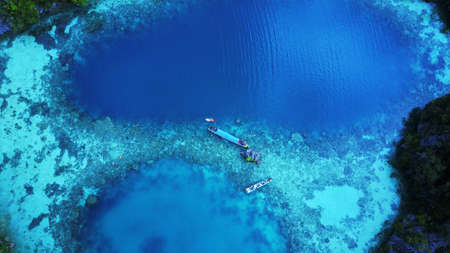 Two boat and a canoe and several snorkeling people on bay with green and blue clear water from top viewの写真素材