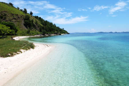 Amazing seashore landscape with white sand, waves crashing, clear tosca colored water and nice green hillsの写真素材