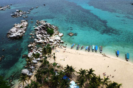 Aerial view of beautiful beach with blue clear water, bunch of artistic rocks, couple of boats and coconut treeの写真素材