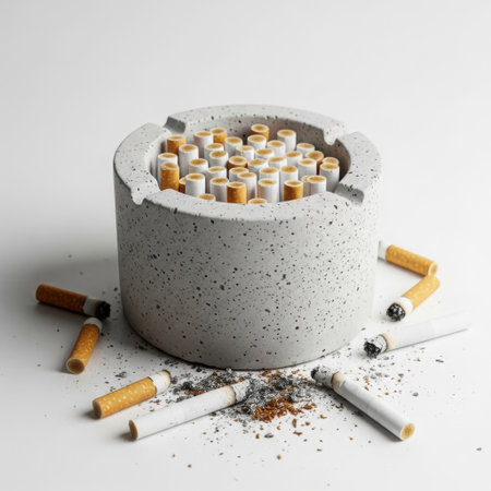 A concrete ashtray is filled to the brim with numerous cigarette butts, ash, and debris, with more scattered around it.の素材
