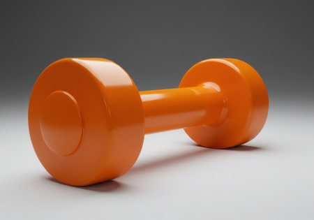 A vibrant orange dumbbell rests against a neutral gray backdrop, symbolizing fitness and exercise. The simple composition highlights the essential tool for strength training and a healthy lifestyle.の素材