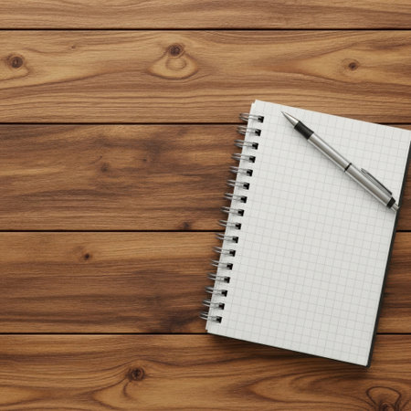A clean, white spiral-bound notebook with a silver pen rests on a textured, brown wooden surface, ready for ideas.の素材