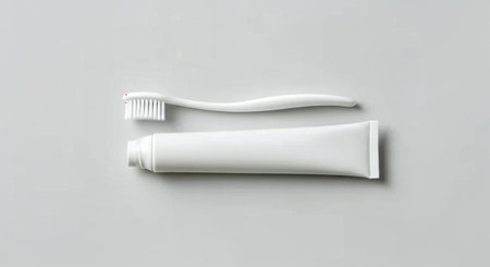 A clean white toothbrush lies next to a white toothpaste tube, both isolated on a plain white background.の素材