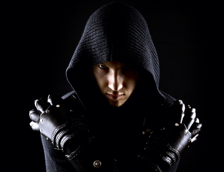 Emotional, young and attractive assassin in gloves on the black background