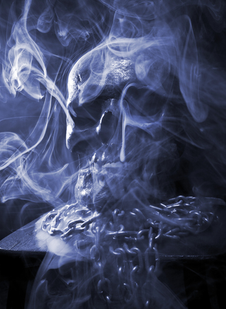 Close up of skull on black background around smoke and with chain.の写真素材