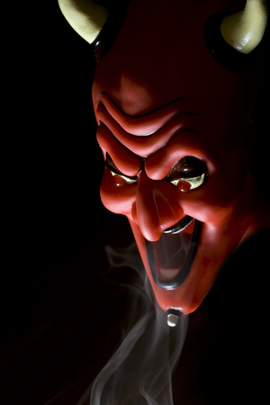 Red mask of devil in smoke on black background.の写真素材