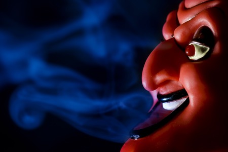 Red mask of devil in smoke on black background.の写真素材