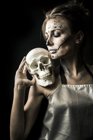Portrait of the woman with halloween makeup close up. Playiong with skull. Isolated image on black background with beautiful studio light.の写真素材