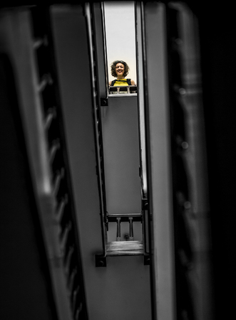 Portrait of woman in yellow shirt standing upstairs and looking down at camera. Soft focus, wooden stairs and a lot of rhythmの写真素材