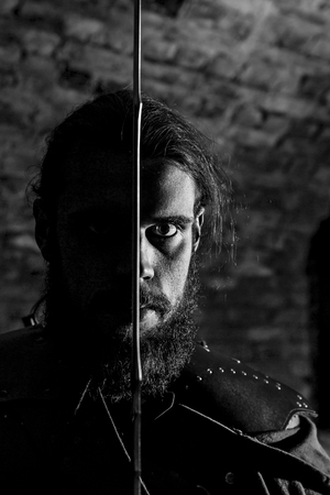Portrait of a man with huge beard close up. He is holding a sword near his face.の写真素材