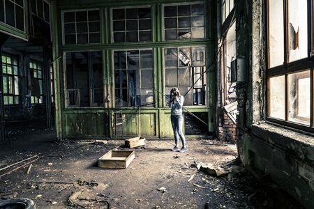 Young girl in old, ruined factory is taking a picture.