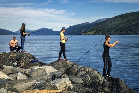 Young people are fishing on the rocks next to the fjord, Norwayの写真素材