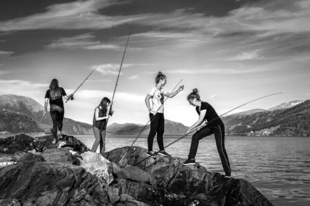 Young people are fishing on the rocks next to the fjord, Norwayの写真素材
