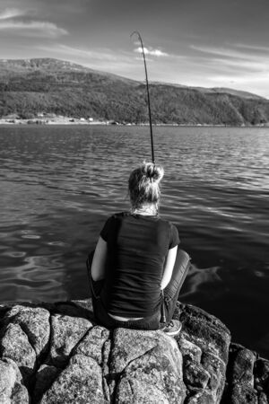 Young woman is fishing in Norway on the fjord.の写真素材