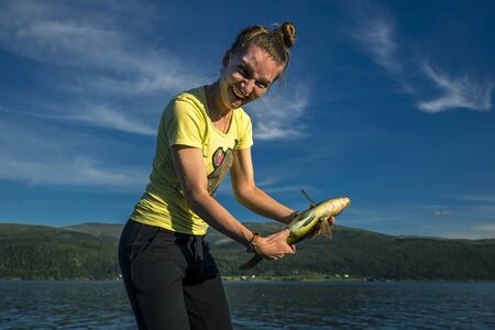 Young woman is fishing in Norway on the fjord, yellow boat on background.の写真素材